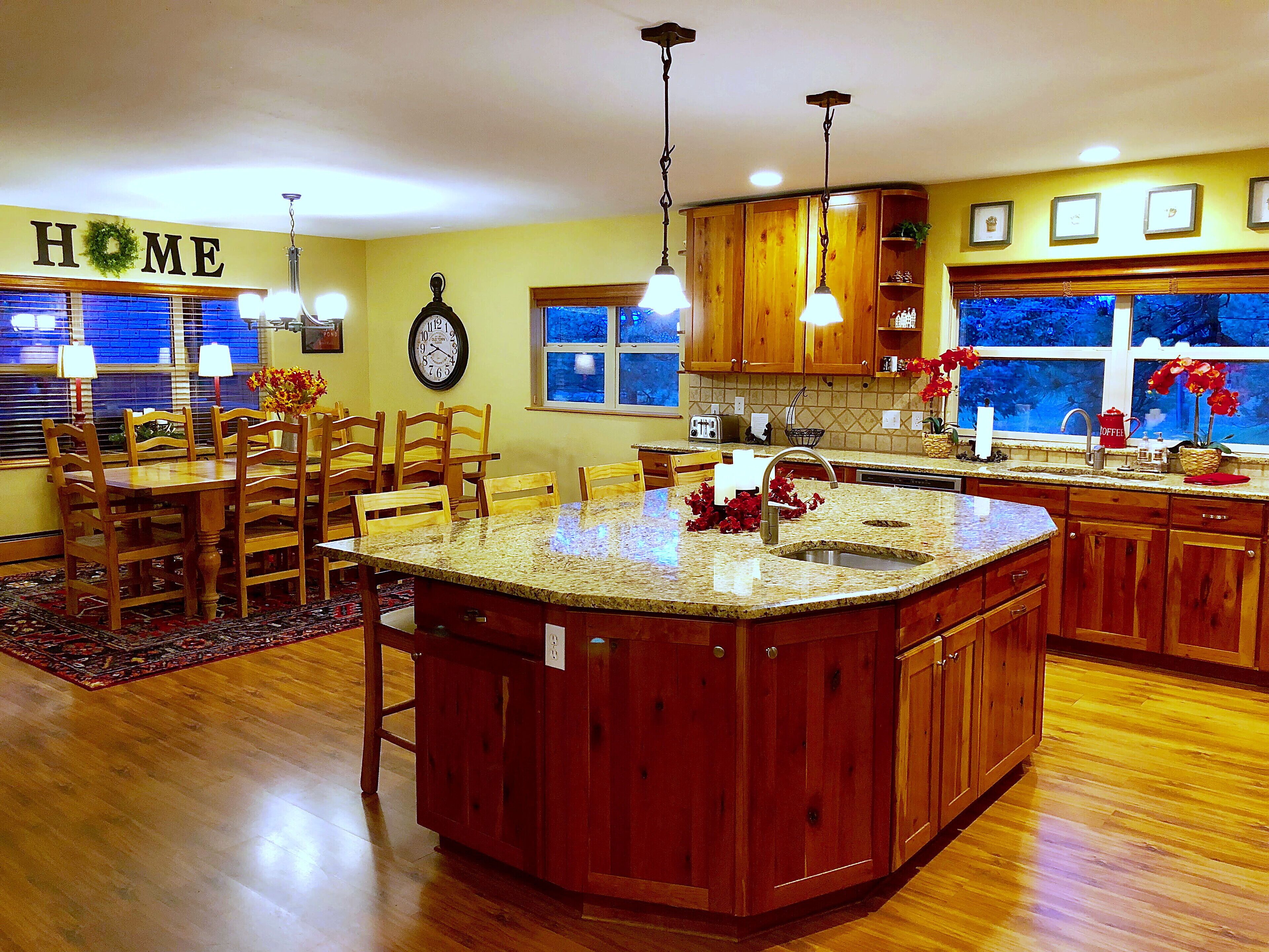 A spacious kitchen with a central island, wooden cabinets, and a dining area with chairs.