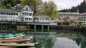 A waterfront property with a row of colorful kayaks docked at the pier, a large building with balconies, and a stone wall. - Custom Waterfront Home near Roche Harbor. Access to Picnic Island. 4-bedrooms. (Friday Harbor)