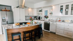 A modern kitchen with white cabinets, a marble countertop, and a built-in island with bar stools. - Custom Waterfront Home near Roche Harbor. Access to Picnic Island. 4-bedrooms. (Friday Harbor)