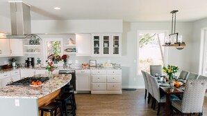 A modern kitchen with a central island, white cabinetry, and a dining area with a chandelier. - Custom Waterfront Home near Roche Harbor. Access to Picnic Island. 4-bedrooms. (Friday Harbor)