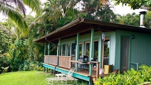 A green house with a porch, surrounded by lush greenery. - Paradise Ocean View Private Cottage Solar Power Tropical Flower Gardens (Hana)
