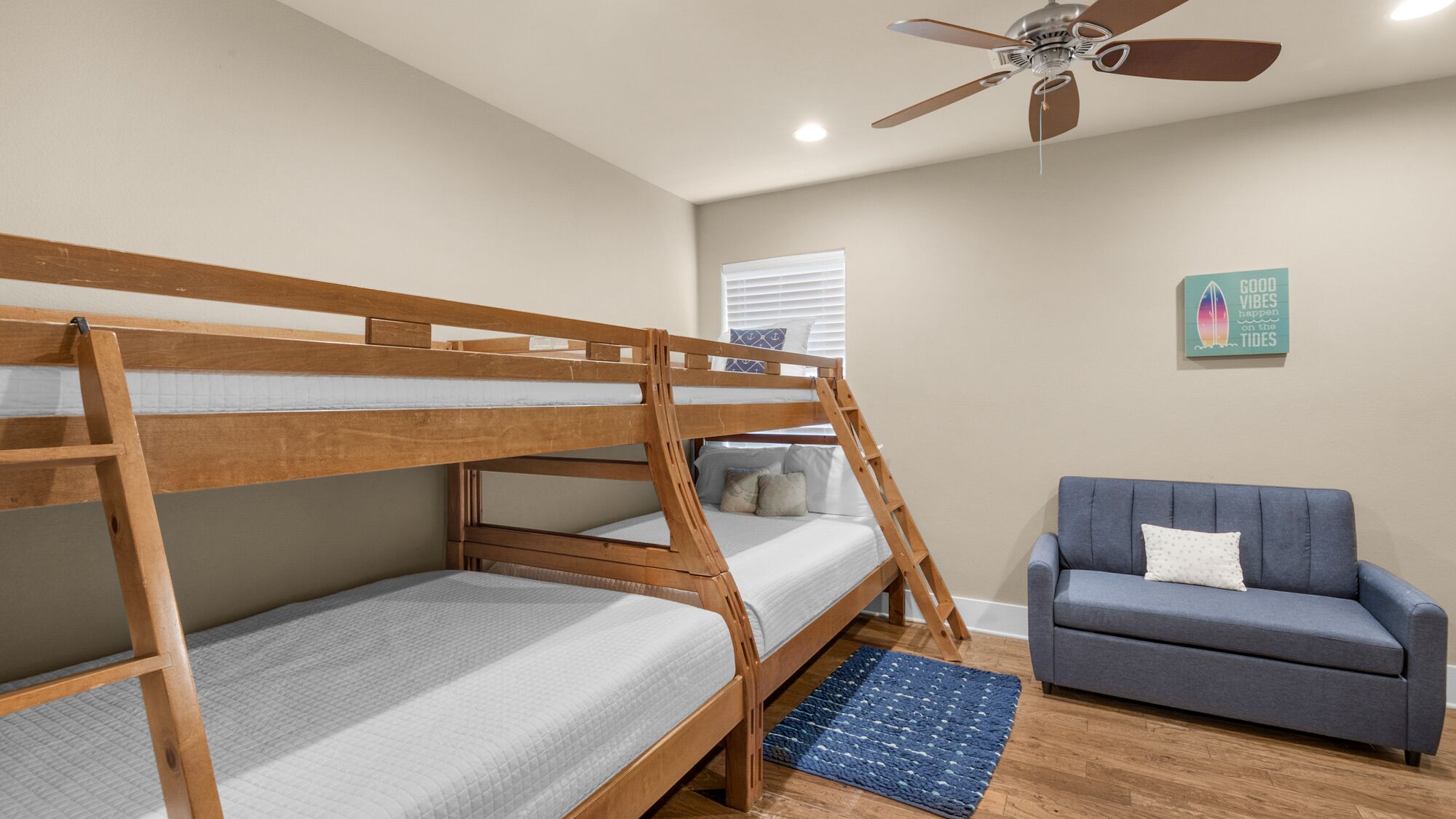 Une chambre avec un lit superposé, un ventilateur de plafond, un canapé bleu et un tapis.