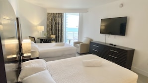 Une chambre d’hôtel avec deux lits, une télévision, un bureau avec une lampe et une vue sur la mer.