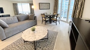 Un salon moderne avec un canapé gris, une table basse ronde et un coin repas comprenant une table et des chaises.