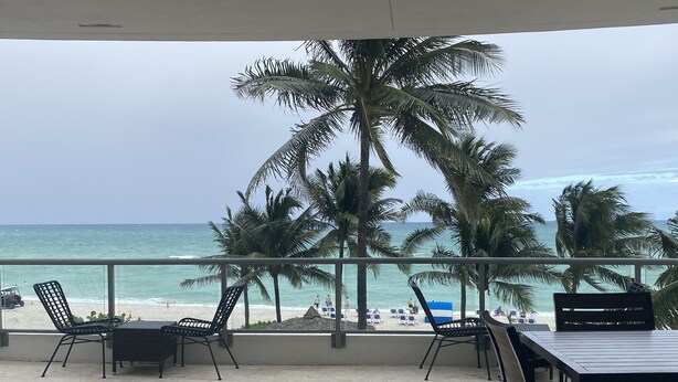 Une terrasse avec vue sur la plage, des palmiers et une table avec des chaises.