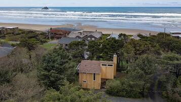 A coastal house with a beach view, surrounded by dense greenery and other residential buildings.
