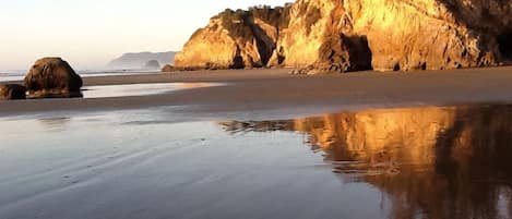 A beach with large rock formations and calm water reflecting the scenery.