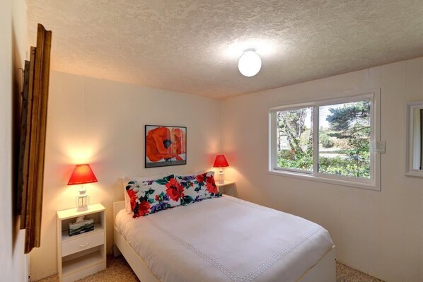 A bedroom with a bed, two bedside lamps, a window, and a ceiling light.