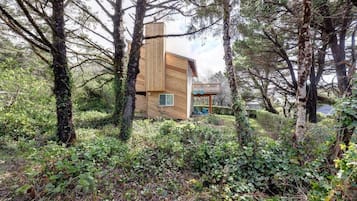 A modern wooden cabin surrounded by dense forest.