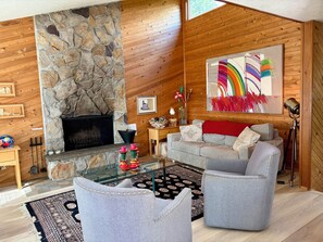 Una sala de estar acogedora con chimenea de piedra, paredes de madera, una mesa de centro de vidrio y un sofá gris.