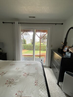 A bedroom with a bed, a dresser, a mirror, and a view through a sliding glass door to an outdoor area.