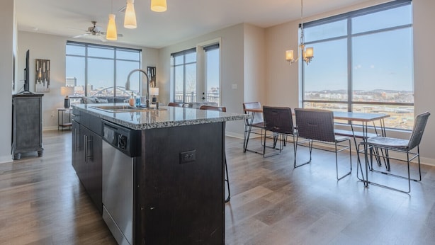 Cocina moderna con una isla grande, comedor con sillas y ventanas amplias que ofrecen vista a la ciudad.