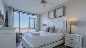 Un dormitorio con una cama grande, mesitas de noche, ventilador de techo y ventana con vistas a la ciudad.