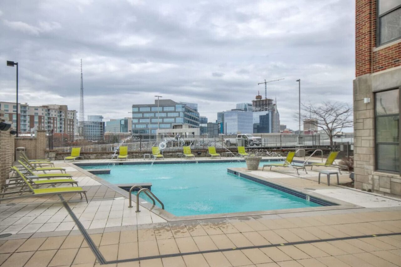 Una piscina en la azotea con varios sillones de sol y una vista panorámica del paisaje urbano.