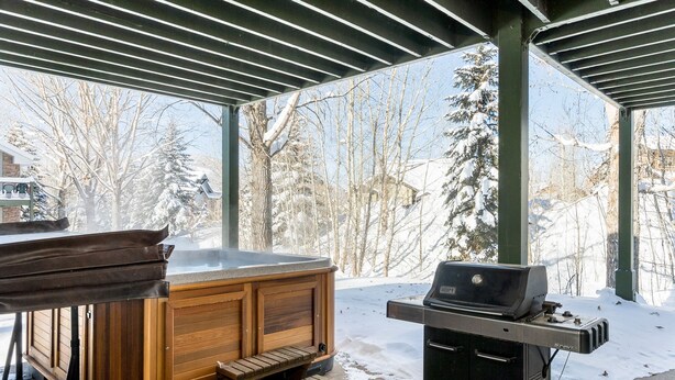 Zona exterior coberta amb banyera hidromassatge, una barbacoa i vista a un paisatge nevado.