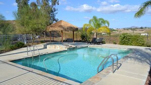 A swimming pool with a wooden deck, lounge chairs, and a thatched-roof structure. - Temecula Winery Estate Villa at Longshadow Ranch Winery             Permit #0204 (Temecula)