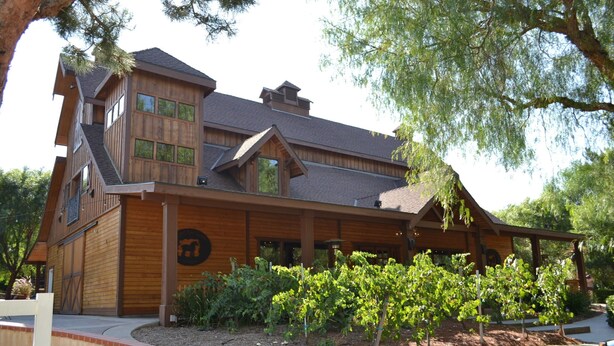 A multi-story wooden building with a covered porch and a vineyard in front. - Temecula Winery Estate Villa at Longshadow Ranch Winery             Permit #0204 (Temecula)