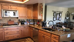 A kitchen with wooden cabinets, a stainless steel microwave, a gas stove, and a dishwasher. There are various kitchen items on the countertop, including bottles and a coffee maker. - Temecula Winery Estate Villa at Longshadow Ranch Winery             Permit #0204 (Temecula)