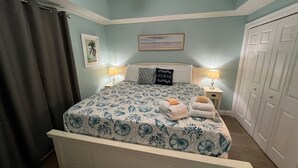A bedroom with a bed, two bedside lamps, a nightstand, a framed picture, and a door.