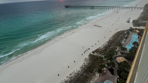 A beach view with a pier, a swimming pool, and a resort area.