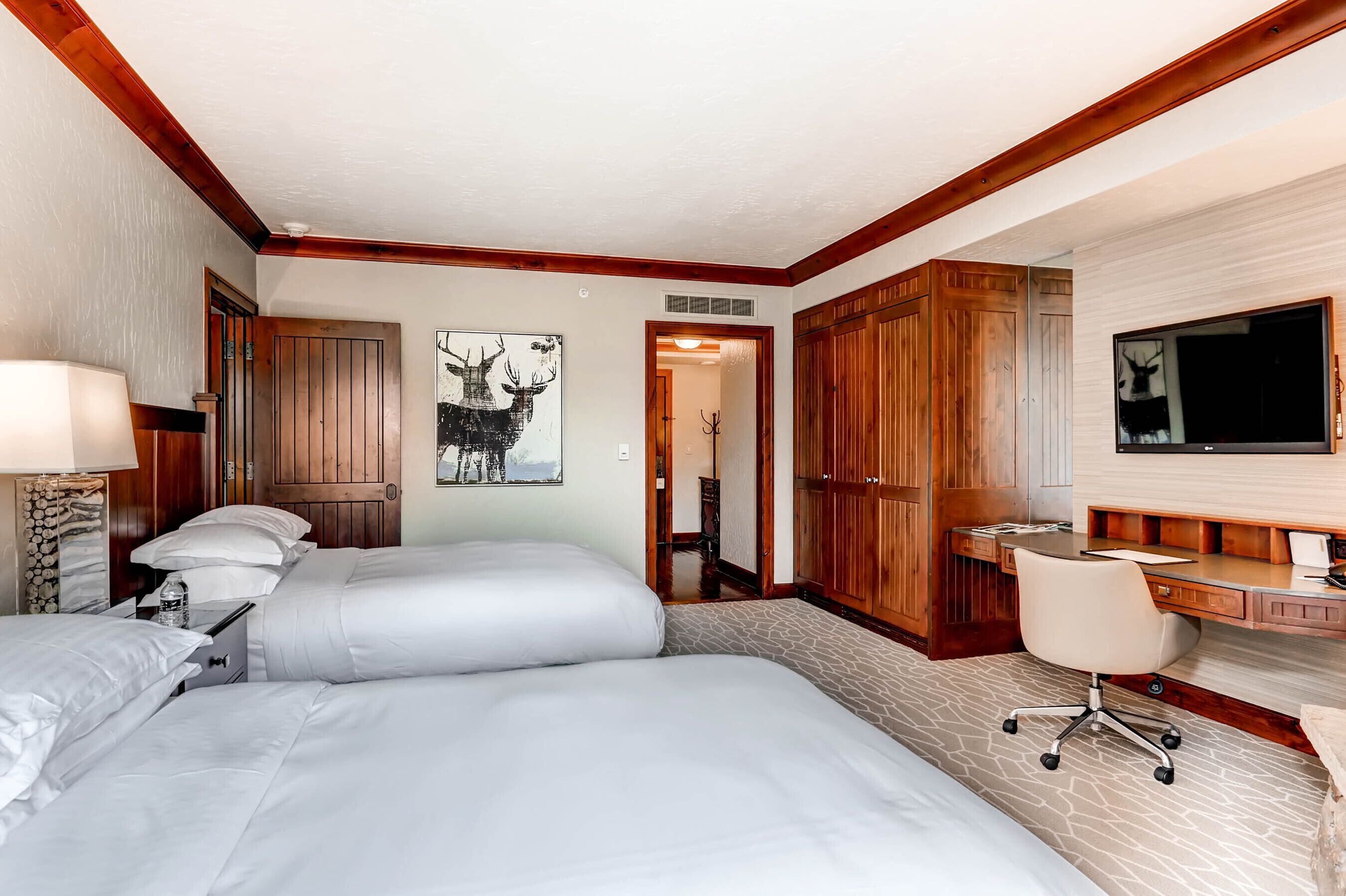 Een hotelkamer met twee bedden, een bureau, een stoel, een televisie en houten lambrisering.
