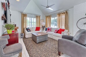 A living room with a sofa set, a coffee table, a patterned rug, a ceiling fan, and a bicycle wheel mounted on the wall. - Walk to Dining,& the Beach–Chic Cottage, Bikes, Kayak, Golf Cart Available (Santa Rosa Beach)
