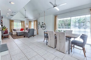A spacious living area with a dining table, chairs, a sofa, and a bicycle hanging on the wall. - Walk to Dining,& the Beach–Chic Cottage, Bikes, Kayak, Golf Cart Available (Santa Rosa Beach)