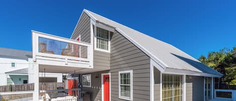 A two-story house with a covered deck, a balcony, and a red door.