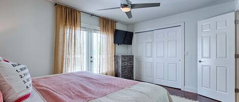 A bedroom with a bed, a ceiling fan, a television, and two doors.