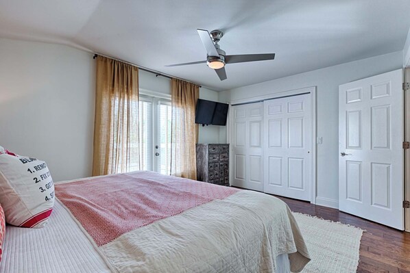 A bedroom with a bed, a ceiling fan, a television, and two doors. - Walk to Dining,& the Beach–Chic Cottage, Bikes, Kayak, Golf Cart Available (Santa Rosa Beach)