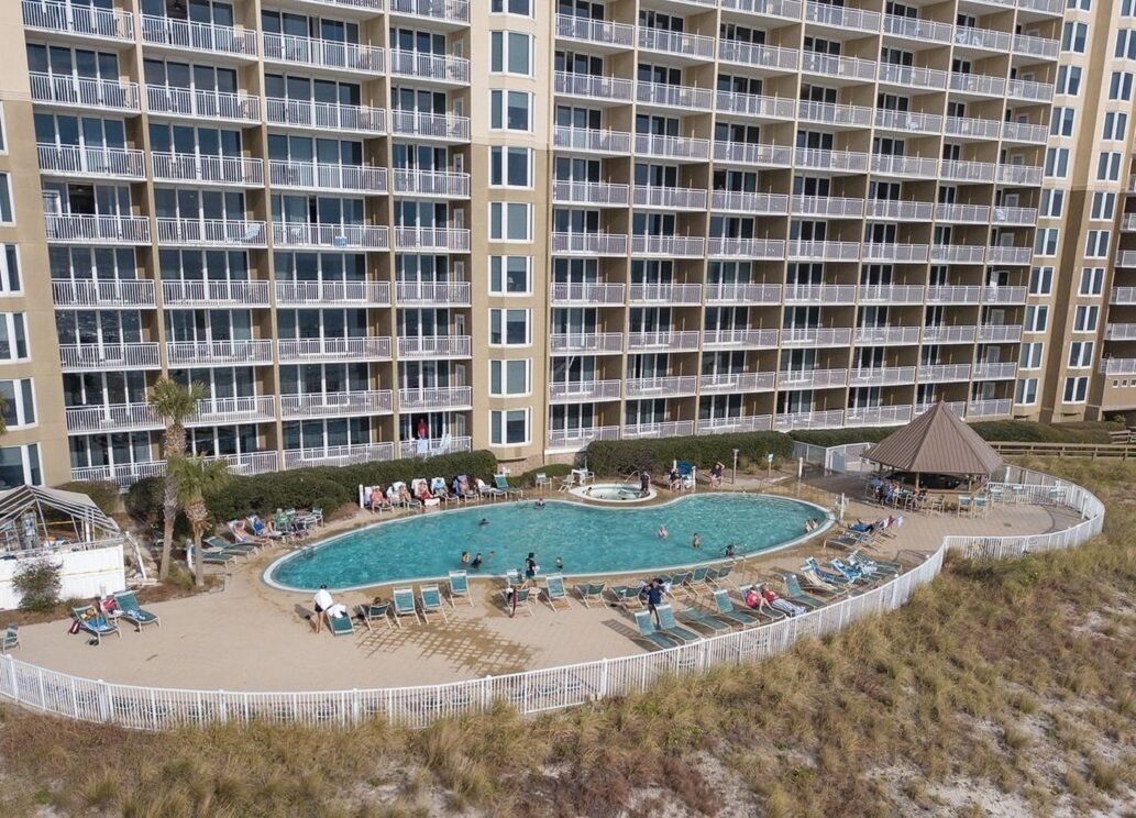 A multi-story hotel with a pool area, including sun loungers and a small pavilion.