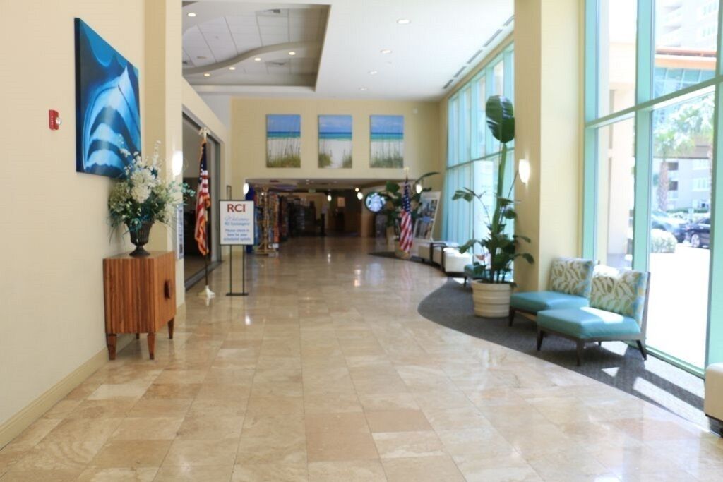 Een hotel lobby met een marmeren vloer, een receptiebalie, een zithoek met een bank en grote ramen.
