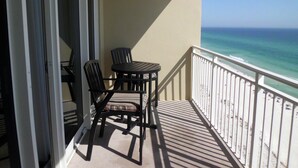 A balcony with a table and chairs, overlooking a beach.