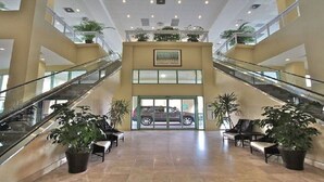 A spacious lobby with two glass staircases, potted plants, and a car parked outside.
