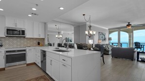 A modern kitchen with white cabinetry, a central island, and a dining area with a view of the sea. -  Gulf Front views- Tower 1-17Th floor-  Pensacola Beach  (Pensacola Beach)