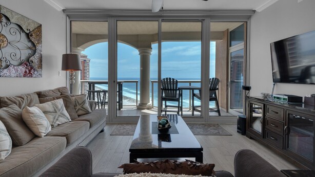 A living room with a sofa, coffee table, and chairs, a television, and a balcony with ocean views. -  Gulf Front views- Tower 1-17Th floor-  Pensacola Beach  (Pensacola Beach)