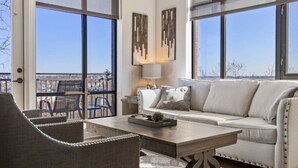A modern living room with a sofa, a coffee table, and a view through large windows.