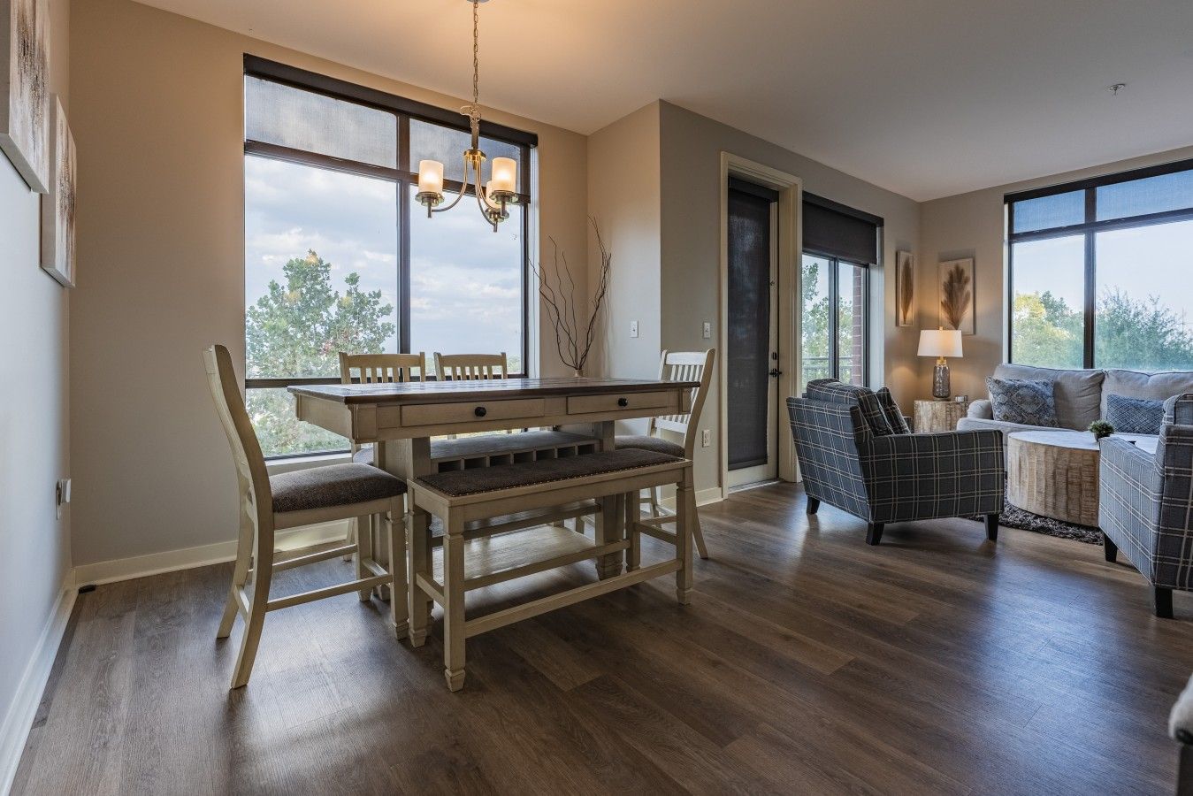 A spacious room with a wooden dining table, chairs, a sofa, and a large window providing a view of the outdoors.