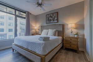 Ein Hotelzimmer mit einem großen Bett, zwei Nachttischen inklusive Lampen, einem Deckenventilator, einem Fenster mit Vorhängen und einem Bild an der Wand.