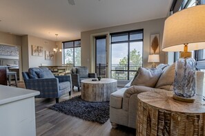 A modern living room with a dining area, large windows, and a view of the outdoors.