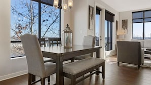 A dining area with a wooden table, cushioned chairs, and a view of trees through large windows.