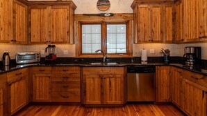 A kitchen with wooden cabinets, a built-in dishwasher, a toaster, and a window with blinds. - Rivamonte by Cottonwood Lodging (Brighton)