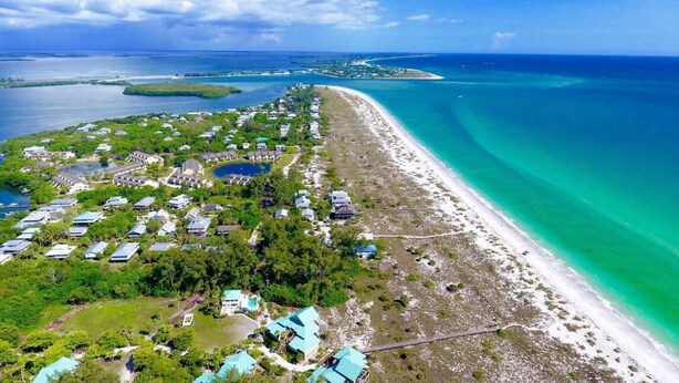 An aerial view of a coastal resort with multiple buildings, a sandy beach, and clear turquoise waters. - Tropical Island Getaway Beachfront Gulf Views-Pool-Ferry & Grocery Delivery incl (Placida)