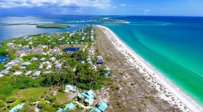 An aerial view of a coastal resort with multiple buildings, a sandy beach, and clear turquoise waters. - Tropical Island Getaway Beachfront Gulf Views-Pool-Ferry & Grocery Delivery incl (Placida)