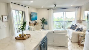 A modern kitchen with a marble countertop, a built-in oven, and a dining area with a white sofa and a glass coffee table. - Tropical Island Getaway Beachfront Gulf Views-Pool-Ferry & Grocery Delivery incl (Placida)