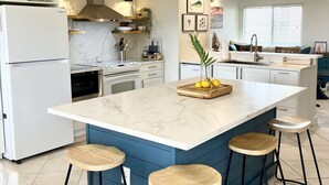 A modern kitchen with a central island, bar stools, and a built-in stove. - Tropical Island Getaway Beachfront Gulf Views-Pool-Ferry & Grocery Delivery incl (Placida)