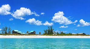 Une propriété située en bord de mer, comprenant plusieurs bâtiments, avec une eau turquoise cristalline et une plage de sable.