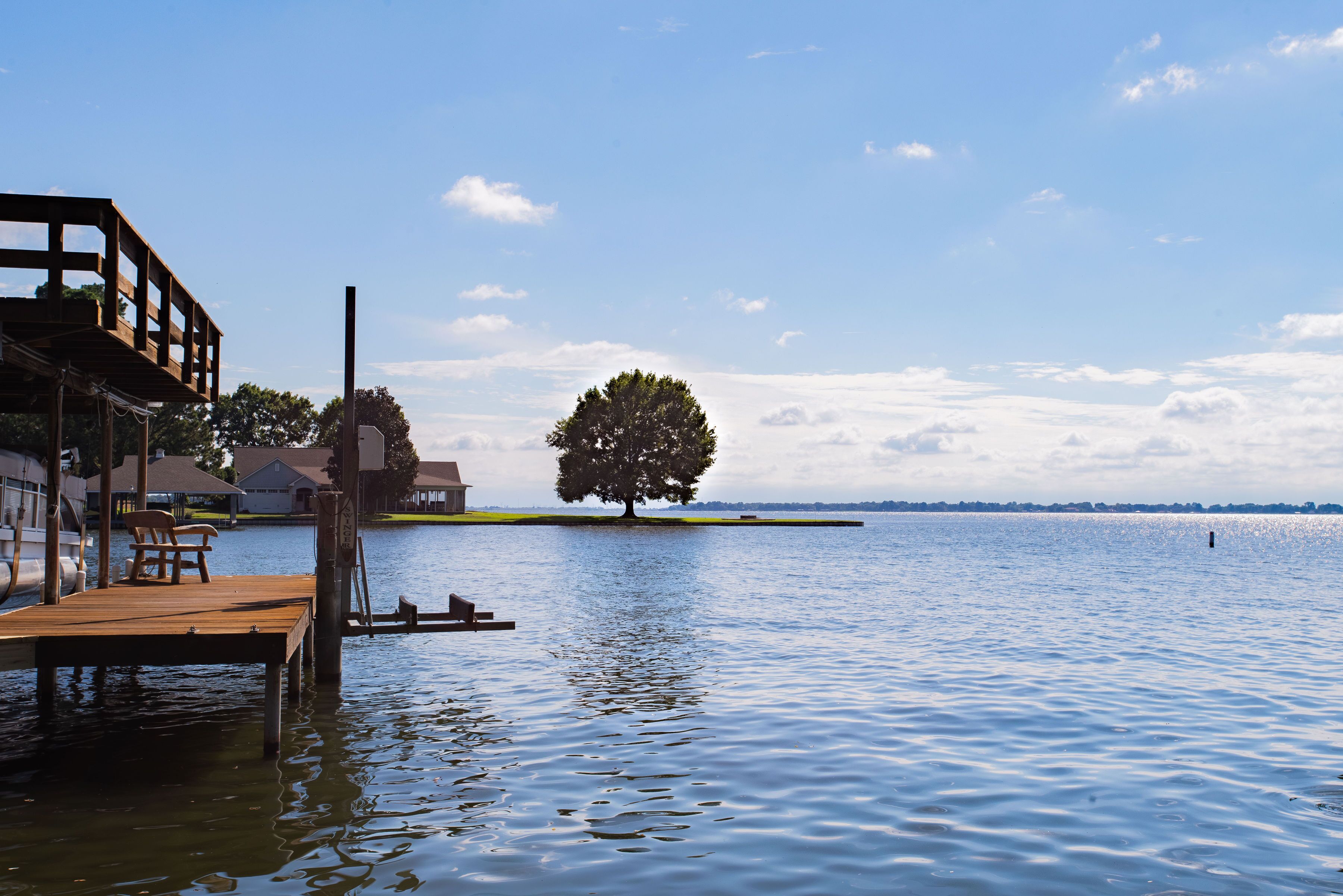 A wooden dock extending into calm water, surrounded by a clear sky and a distant tree.
