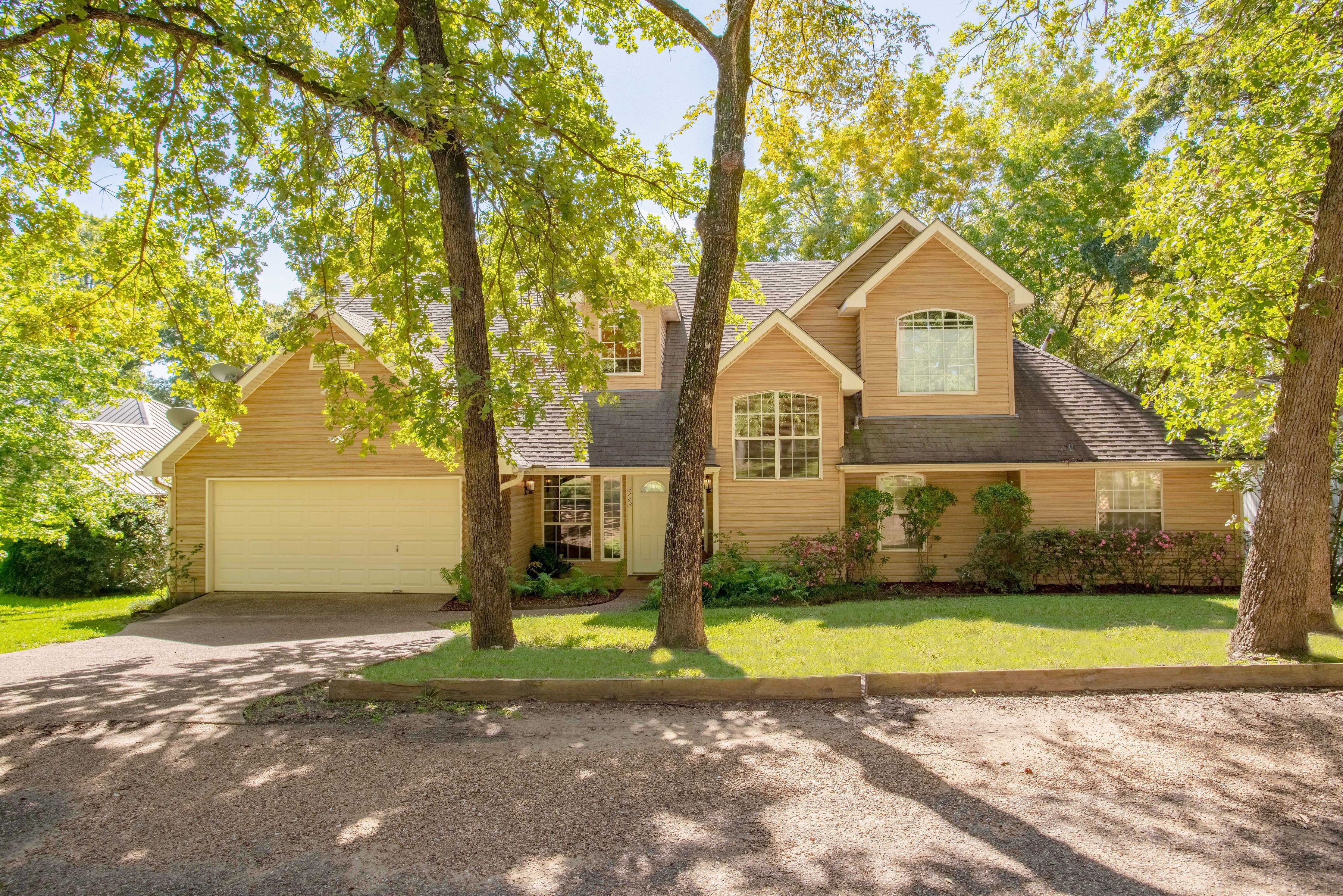 A two-story house with a garage, surrounded by trees and a well-maintained lawn.