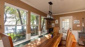 A dining area with a long wooden table, large windows, and a view of the outdoors.